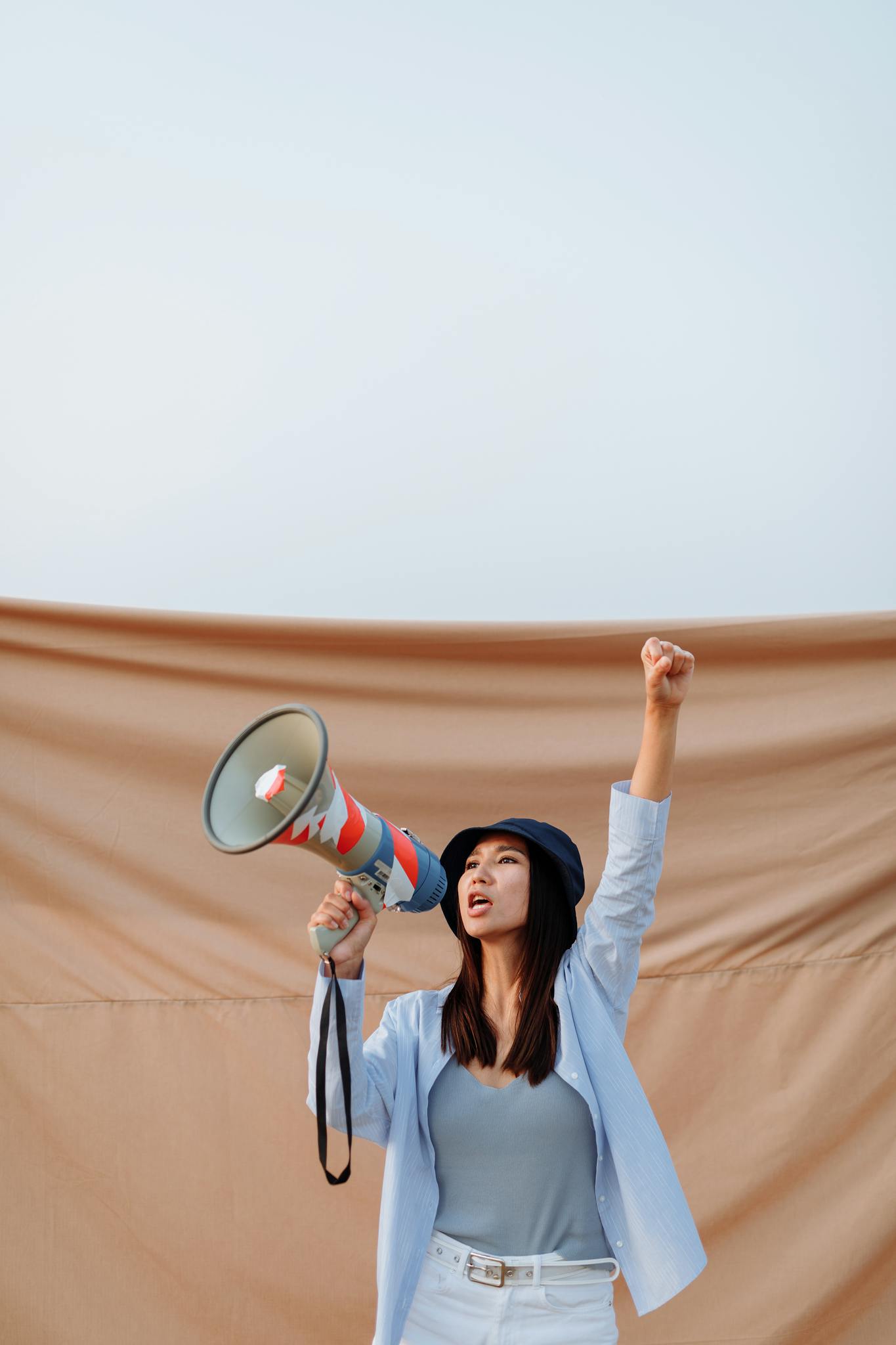 Jeune femme déterminée avec un mégaphone, levant le poing en signe de protestation, illustrant la mission d’une plateforme féminine engagée.