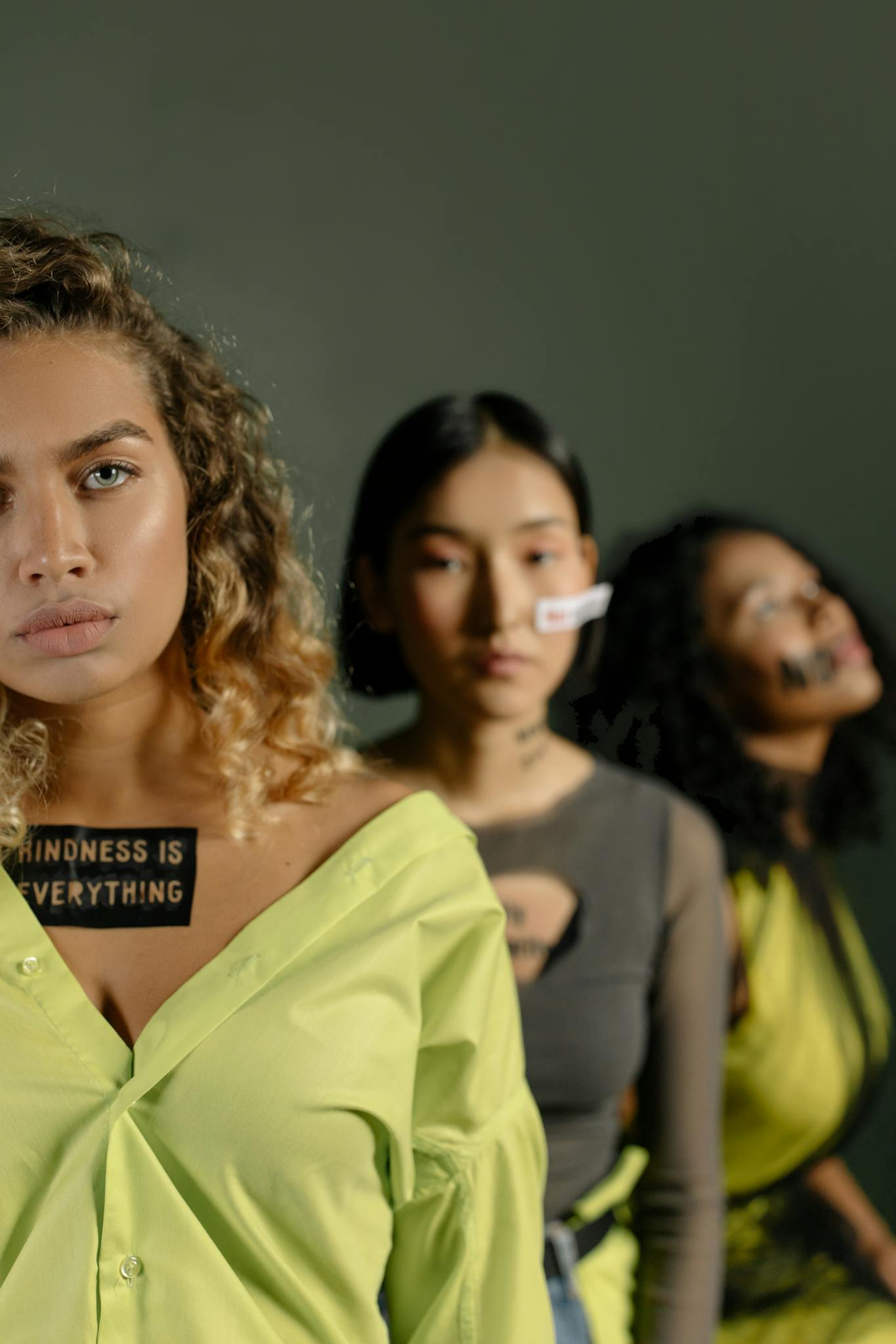 Three diverse women advocating kindness and unity with slogan patches.